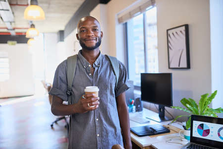 A Black trendy man arrives at the office with his coffee and backpackの写真素材