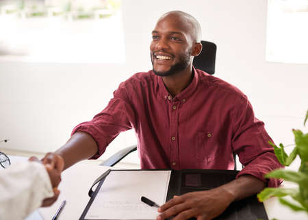 A Black businessman greets a client from his office desk for in person meetingの写真素材