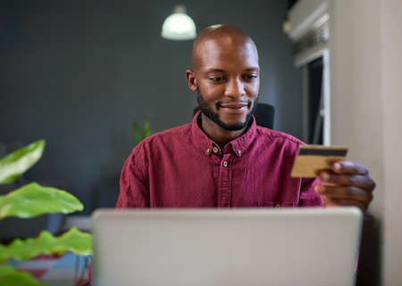 A Black man shops online from his office desk with credit card