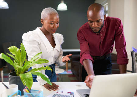 Two Black colleagues discuss work presentation on laptopの写真素材