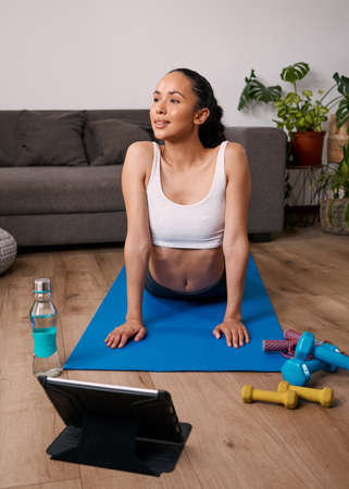 A young woman stretches in upward facing dog during home virtual workout