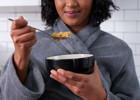 A close up of cornflakes on a spoon while woman eats breakfast in gownの写真素材