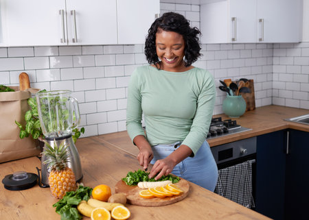 A young multiracial woman chops fruit and spinach for green smoothieの写真素材