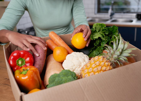 An anonymous young woman checks her fruit and veg delivery boxの写真素材