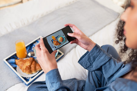 A young woman takes photo of her breakfast platter in bed with cellphone cameraの写真素材