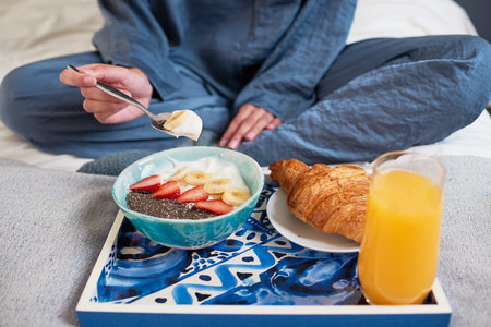 Close up of young woman eating breakfast bowl in bed in pajamasの写真素材