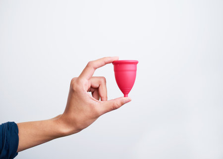 Close up of hand holding pink menstrual cup against white backgroundの写真素材