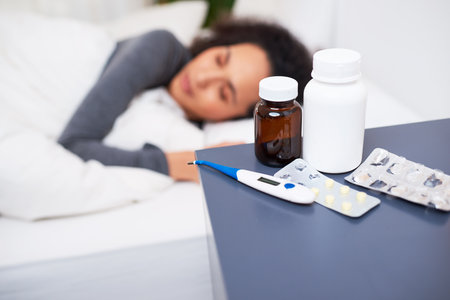Selective focus on bedside table of sick woman with pill bottles and thermometer