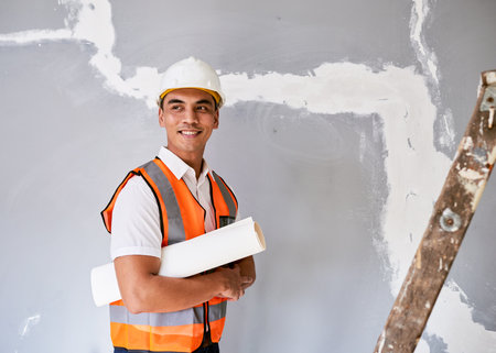 An attractive Asian construction worker holds building plans under his arm