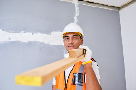 A young Filipino construction worker carries wooden planks on shoulder on siteの写真素材