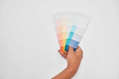 Close up of a hand holding pastel coloured paint swatches against pale grey wallの写真素材