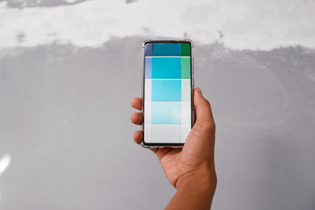 Close up of hand holding cellphone with digital paint swatch against grey wallの写真素材