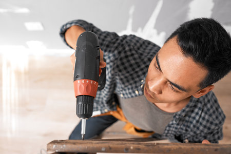 Selective focus on drill while young Asian man drills into wood - overhead shotの写真素材