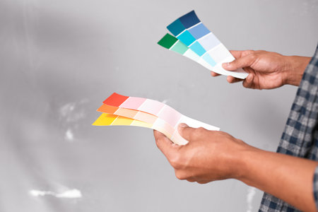 Close up of hands holding bright coloured paint swatches against grey wallの写真素材