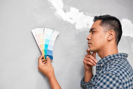 An Asian man contemplates which paint swatch will work on newly renovated wallの写真素材
