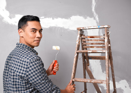 A young Asian man looks serious as he prepares to paint cracked wallの写真素材