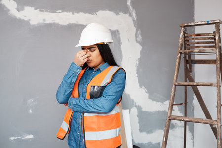 A young South Asian construction worker rubs her sinuses in pain, headacheの写真素材