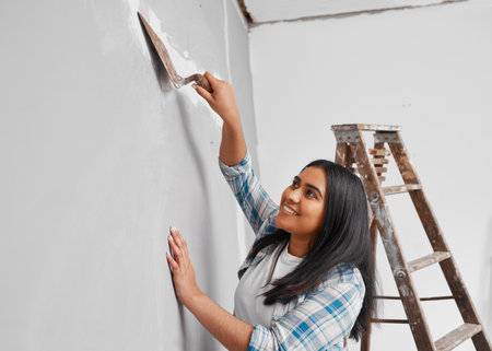 Young Indian woman plasters over cracks in wall home DIY projectの写真素材