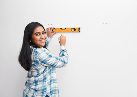 A young woman smiles while using spirit level against wall doing home DIY