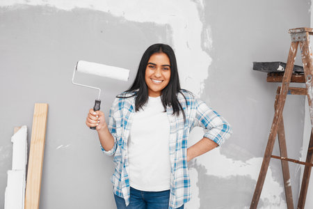 Young Indian woman poses with paintbrush roller getting ready to paint wallの写真素材