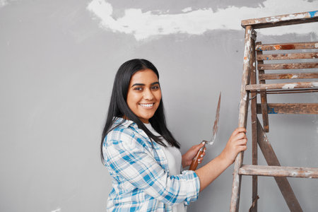 Young Indian woman plasters over cracks in wall home DIY projectの写真素材