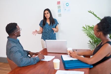 Indian woman leads meeting in the office boardroom, gesture explain to colleague