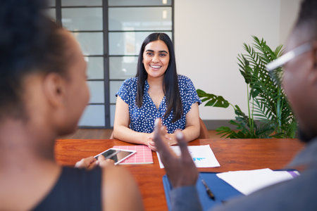 Three business colleagues sit around conference table, meeting smile discussの写真素材