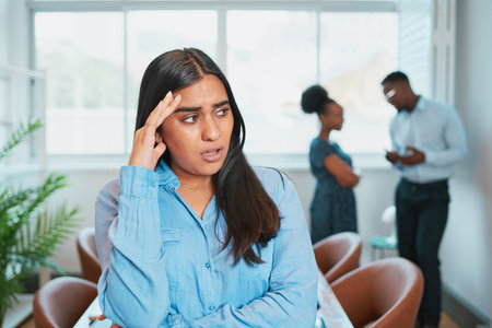 Young woman looks upset while colleagues talk behind her back, office dramaの写真素材
