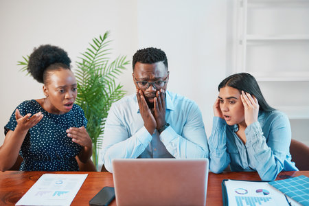 Three colleagues look shocked at laptop screen, project failure, crash, bad newsの写真素材