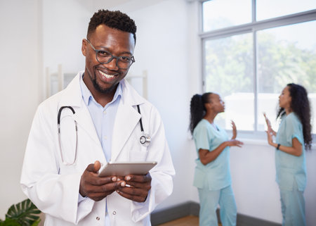 Portrait of Black doctor holding digital tablet, with nurses in backgroundの写真素材