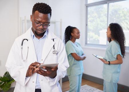 Portrait of Black doctor holding digital tablet, with nurses in backgroundの写真素材