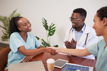Two doctors shake hands while colleague claps, medical promotion achievementの写真素材