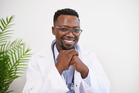 Close up portrait of a Black doctor sitting at his desk smiling, hands clasped