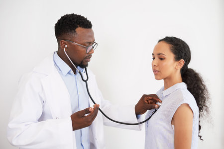 Black male doctor listens to female patients heartbeat, tells her breathe inの写真素材