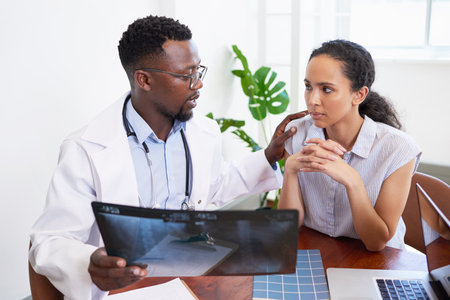 Black male doctor explains x-ray results to young worried patient in officeの写真素材