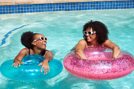 Two Black friends practice kicking in the swimming pool with inflatable rings