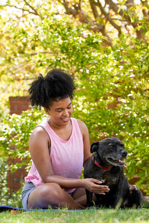 A multi-ethnic woman and her happy dog, giving attention in the park pet ownerの写真素材