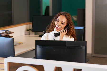 Front desk receptionist laughs on the phone, multi-ethnic woman with curly hairの写真素材