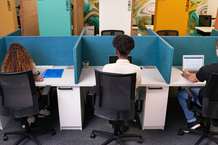 Three young people share coworking space, work side by side with desk dividers