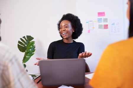 Black woman with afro smiles at meeting, development team coding, laptopの写真素材