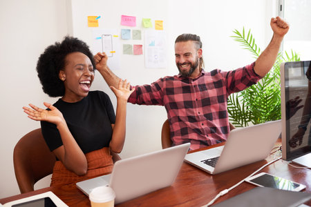 Two developers cheer with arms raised in office, successful launch of productの写真素材