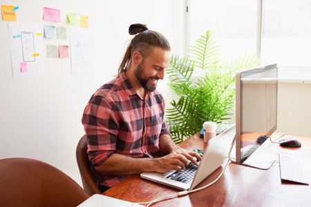 Senior developer works in open plan creative office, man bun hipster look