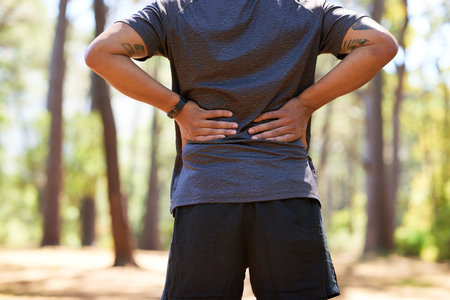 Back view of Asian man with hands on lower back, muscle pain taking a breakの写真素材
