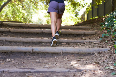 Cropped view of young woman running up trail steps in park, training outdoorsの写真素材