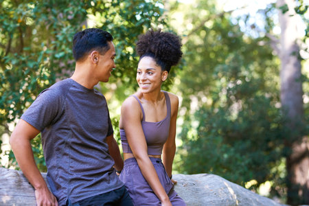 Beautiful couple taking break on hike through forest, sitting on log talkingの写真素材