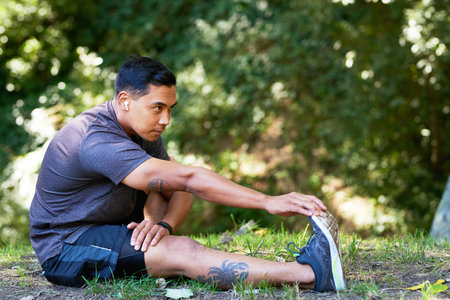 Attractive Asian man stretches calf muscle in park after trail run, cool downの写真素材