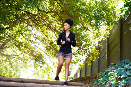 Wide view of young multi-ethnic woman running on trail in park, serious and fit