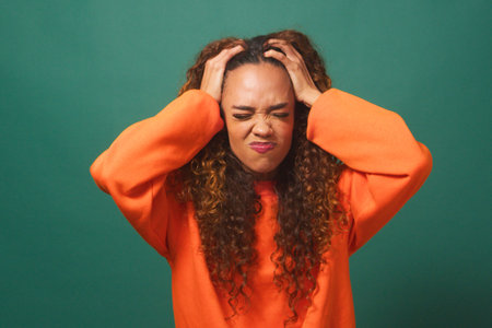 Frustrated and angry young woman tears hair out - green studio backgroundの写真素材