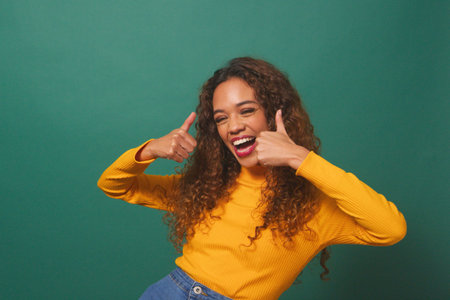 Beautiful multi-ethnic woman gives double thumbs up, green studio backgroundの写真素材