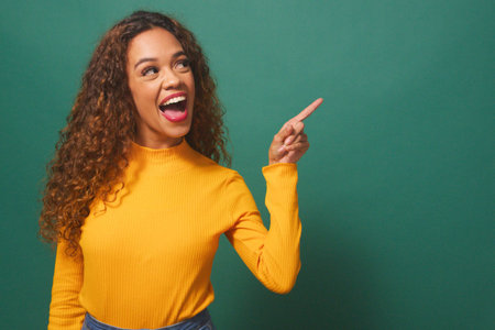Beautiful young woman points to copy space right, excited, sale, green studioの写真素材
